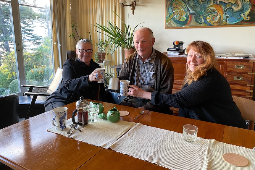 Two middle aged women and an elderly man sitting at a table drinking coffee.