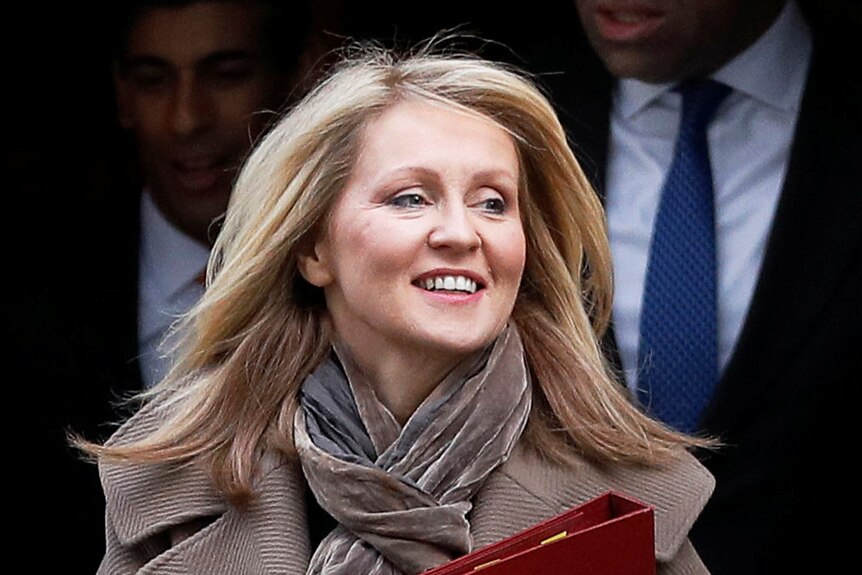 A blonde woman wearing a coat and scarf smiles as she leaves number 10.