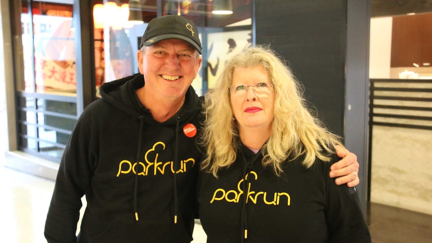 Man and woman in athletic wear smile at photographer