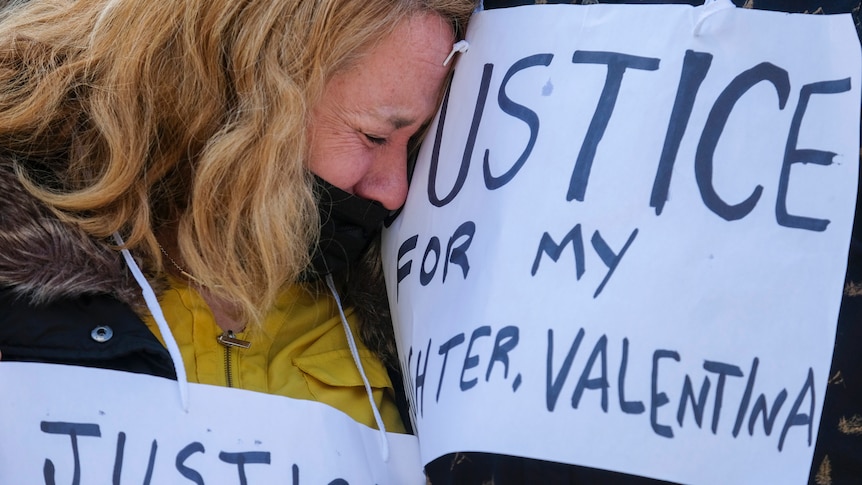 A close up of the mother of Valentina Orellana-Peralta, crying into hand-written signs that say "justice for my daughter".