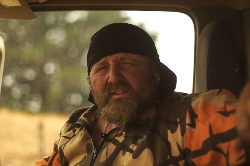 A man with beard sits in his truck from which he has been fighting fires