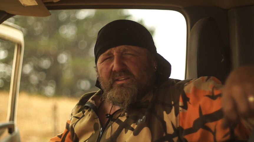 A man with beard sits in his truck from which he has been fighting fires