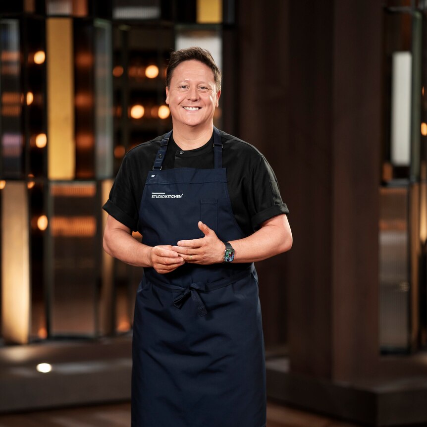man wearing black clothes and a blue apron smiling