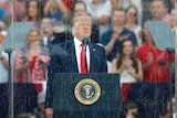Donald Trump looking morose while standing behind wet bulletproof glass