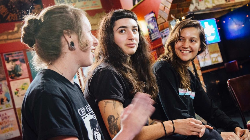 Three members of Camp Cope sit at a bar.