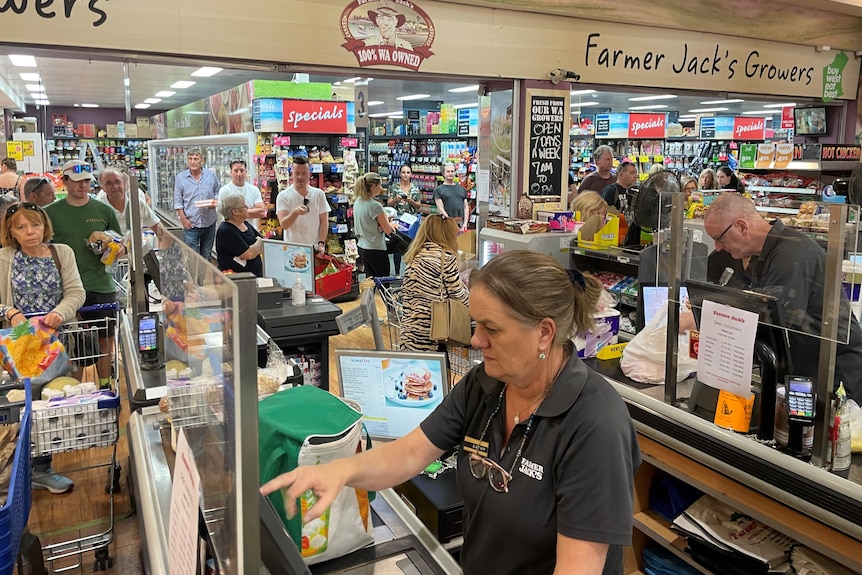 A woman behind the cash registers at a very busy supermarket.