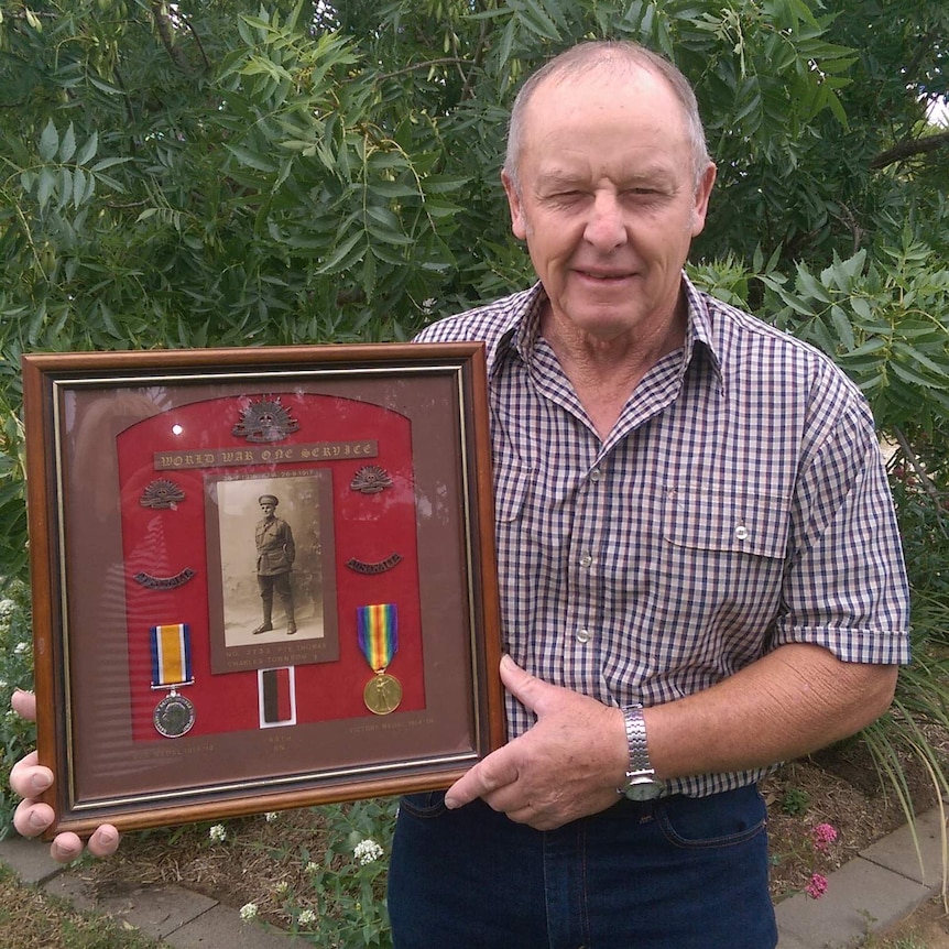 Ken in a background, holding a framed portrait and medals of Thomas Charles Townrow