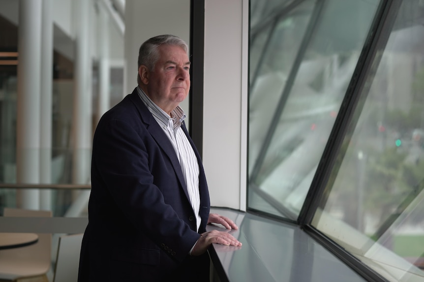 A portrait of a man wearing a suit looking out an office window