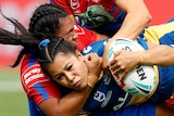 A Parramatta NRLW player is tackled by Newcastle Knights players.