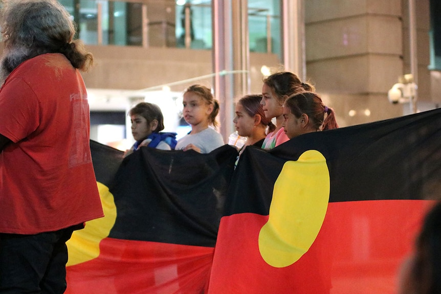 Children holding the Aboriginal flag at a night-time vigil for Elijah Doughty.