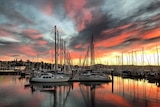 Multi coloured clouds over still water with a line of yachts with sails down