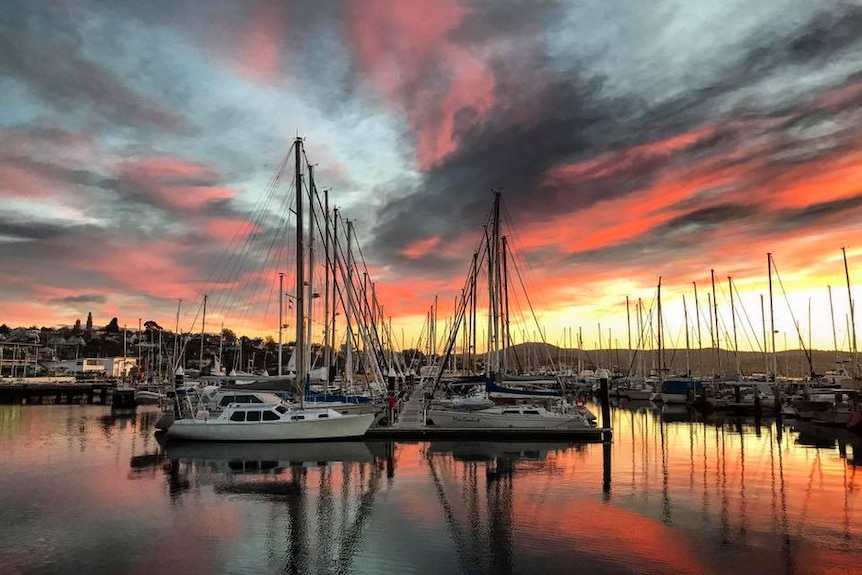 Multi coloured clouds over still water with a line of yachts with sails down