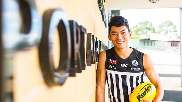 A football player leans against a wall holding a football