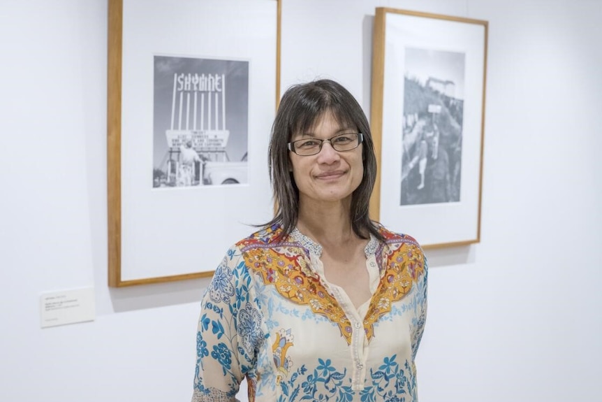 Woman with brown shoulder length hair and olive skin smiles in an art gallery.