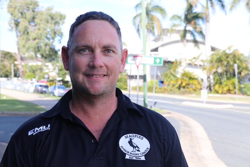 A middle-aged man wearing a black shirt smiles at the camera on a street corner