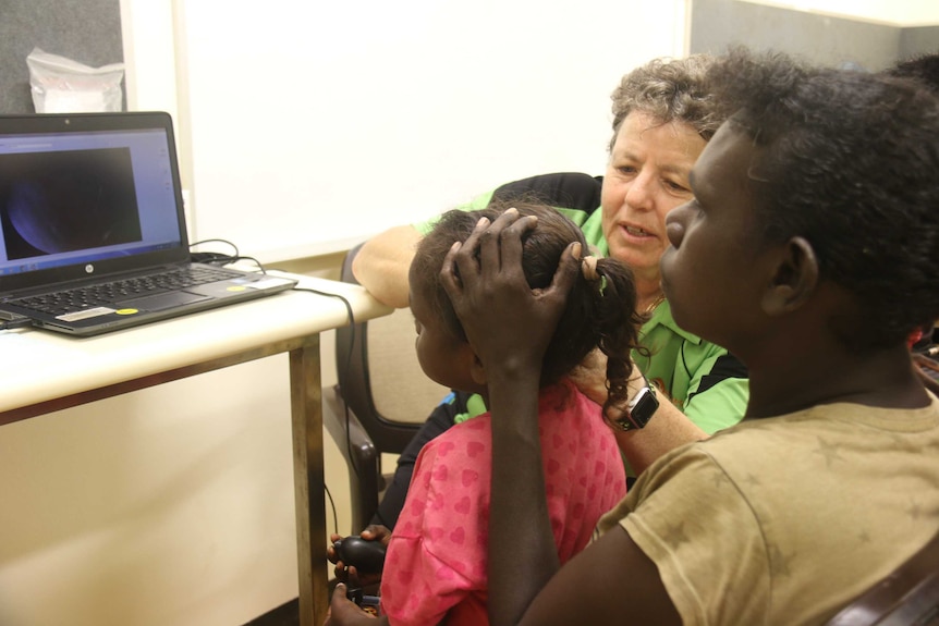 A four-year-old girl sits on her mother's lap while a nurse puts a camera in ear.