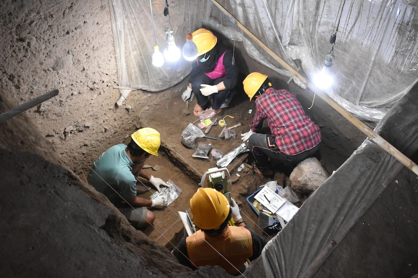 People in hardhats sitting at the bottom of a square pit