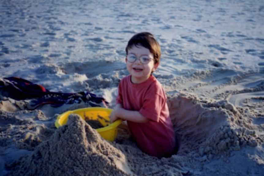 A young boy smiles for the camera while digging a hole on a beach