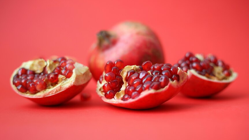 pomegranate fruit cut open in 3 pieces showing red pulp inside