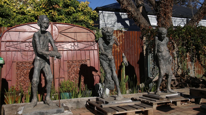 Three brass sculptures of men stand against the wall.