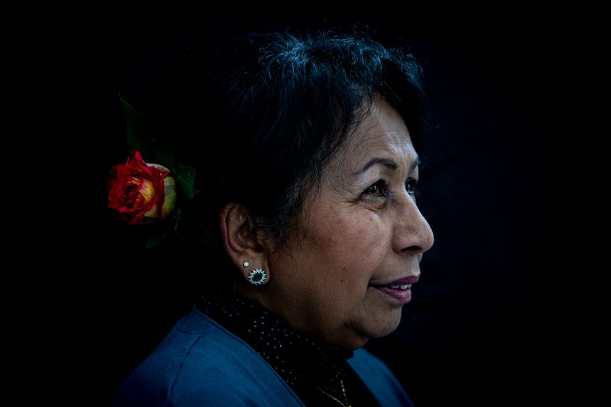 A beautiful close-up portrait of Thit Tieu, who is wearing a red flower in her dark hair and smiling slightly.