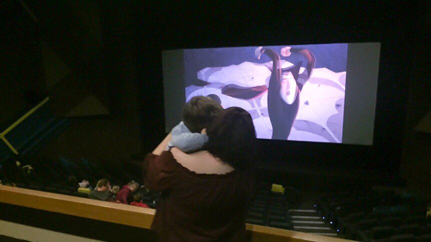 A mum holds her young son while standing up in a theatre during a movie screening.