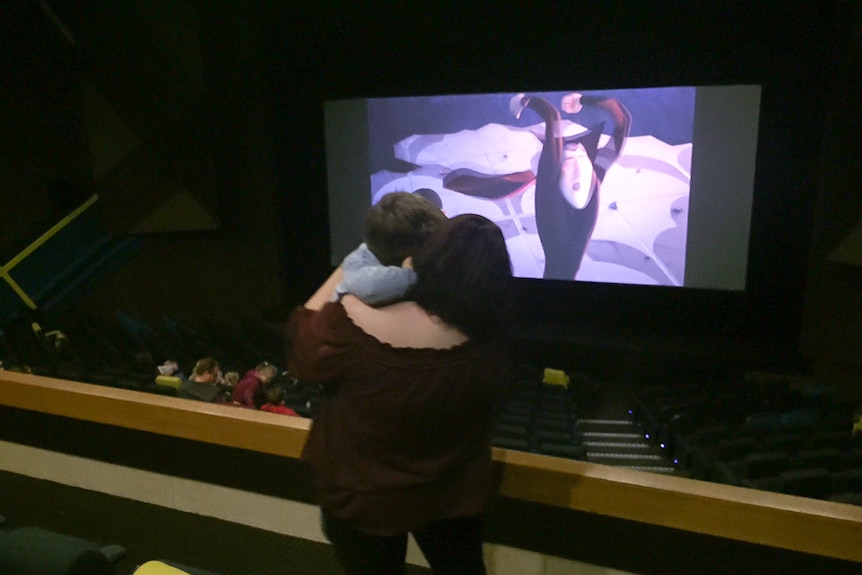 A mum holds her young son while standing up in a theatre during a movie screening.