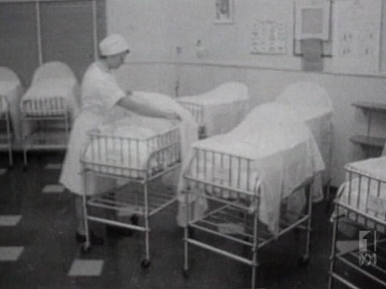 A black and white photo of a nurse putting a baby in a cot.