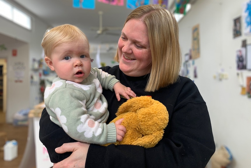 A woman wearing a black jumper holds a child wearing a green jumper.