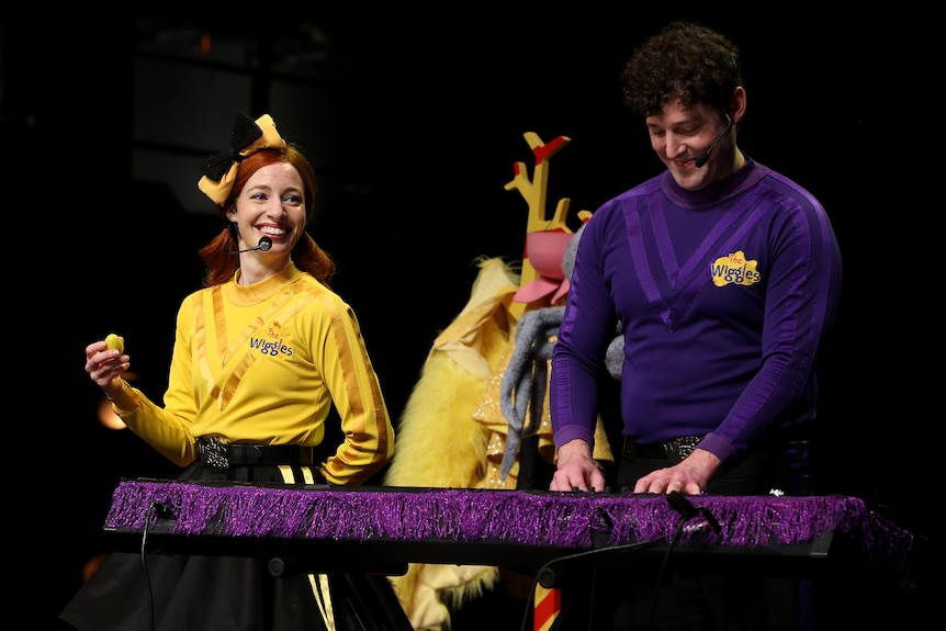 A woman in yellow and man in purple standing at a keyboard.