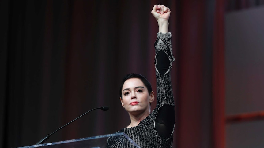 Actress Rose McGowan powerfully raises her fist in the air and stares out at the crowd