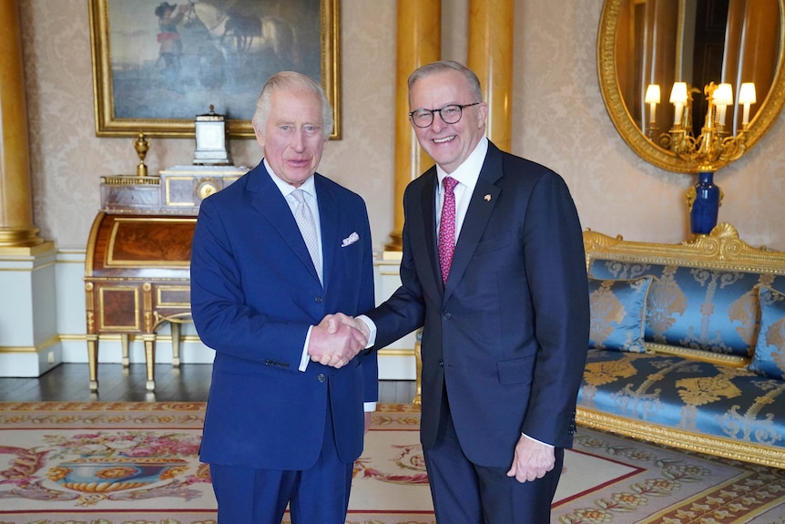 King Charles and a smiling Anthony Albanese look at the camera as they shake hands