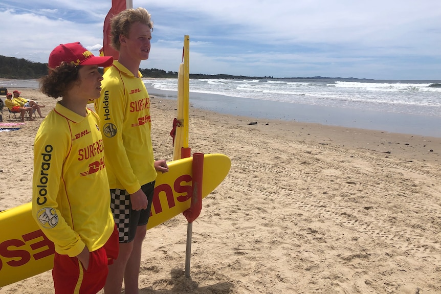 Two teenage boys in lifeguard uniforms overlook the beach. 