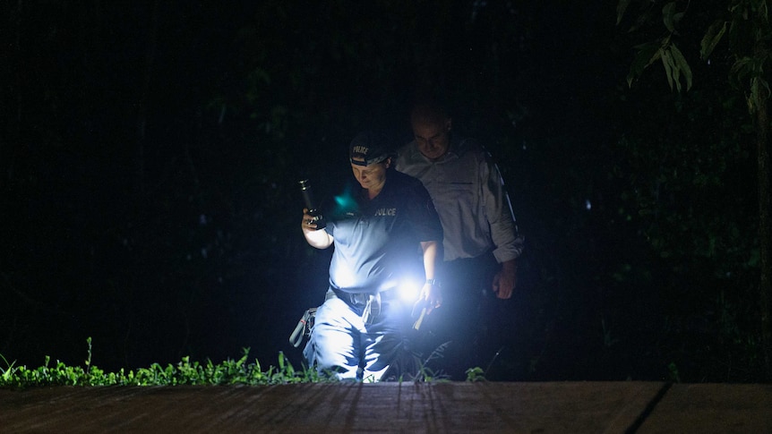 Northern Territory police officers are using flashlights in the dark and wearing uniform.