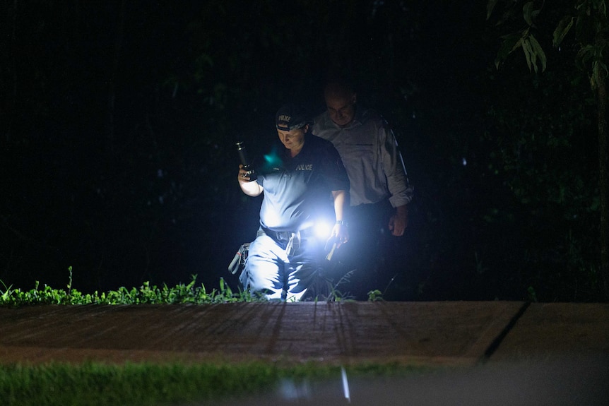 Northern Territory police officers are using flashlights in the dark and wearing uniform.