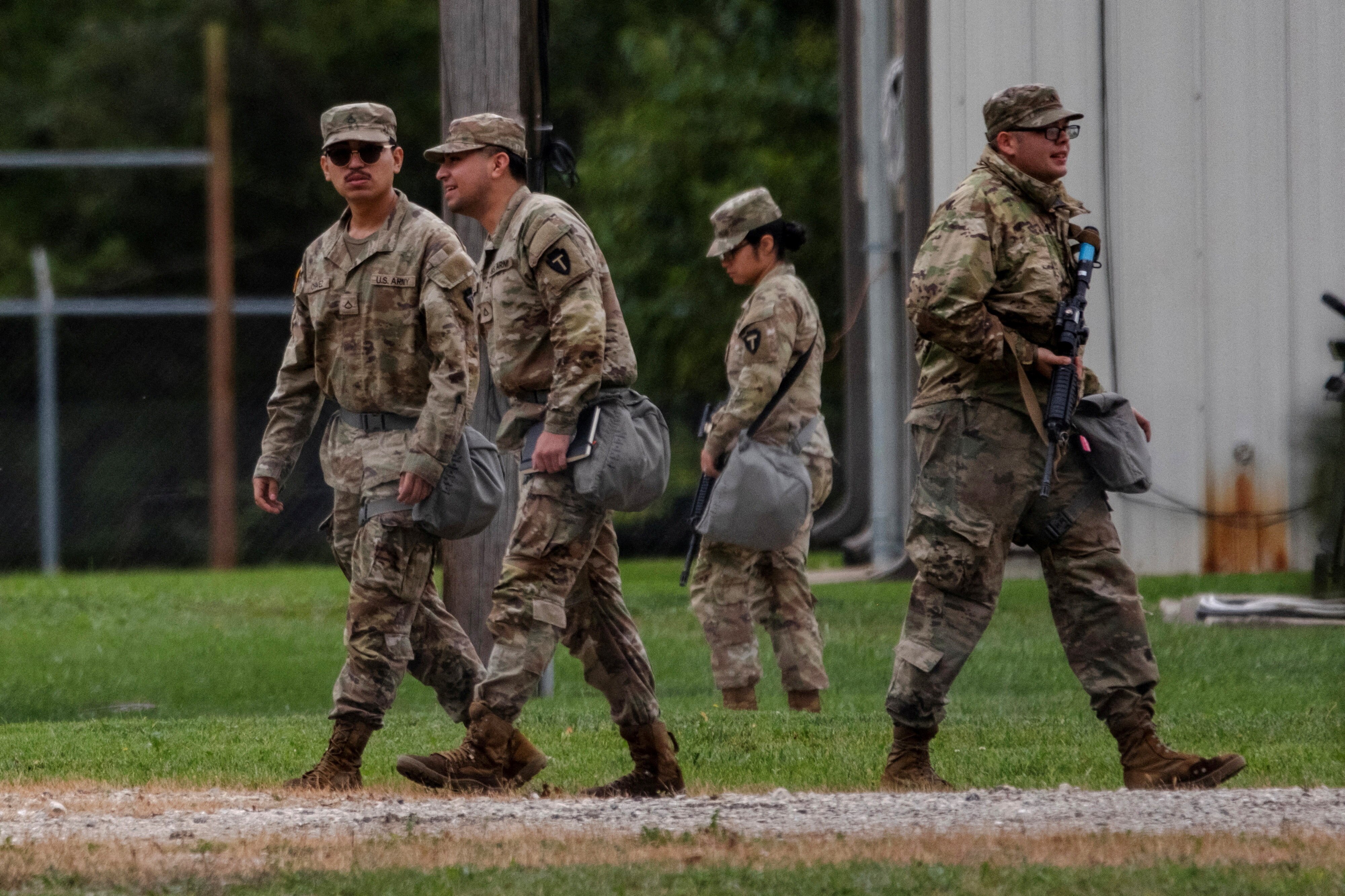 A group of troops wearing camo fatigues and carrying guns walk down a path.