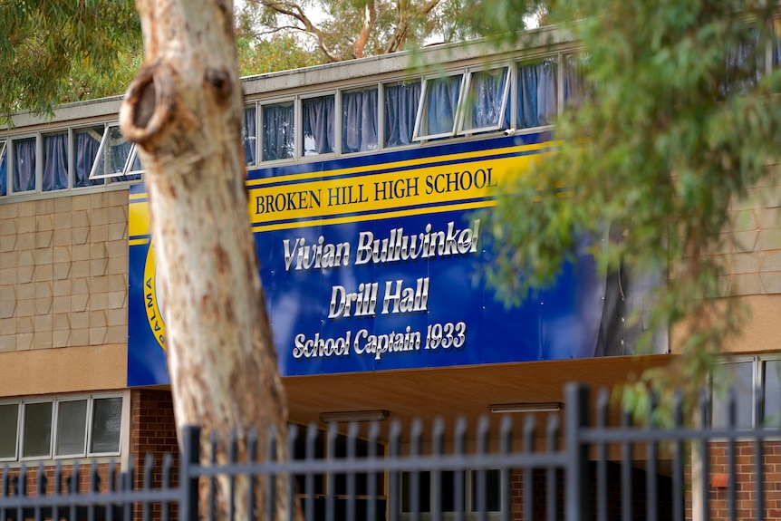 A blue and yellow sign saying 'Broken Hill High School' with a trees next to it 
