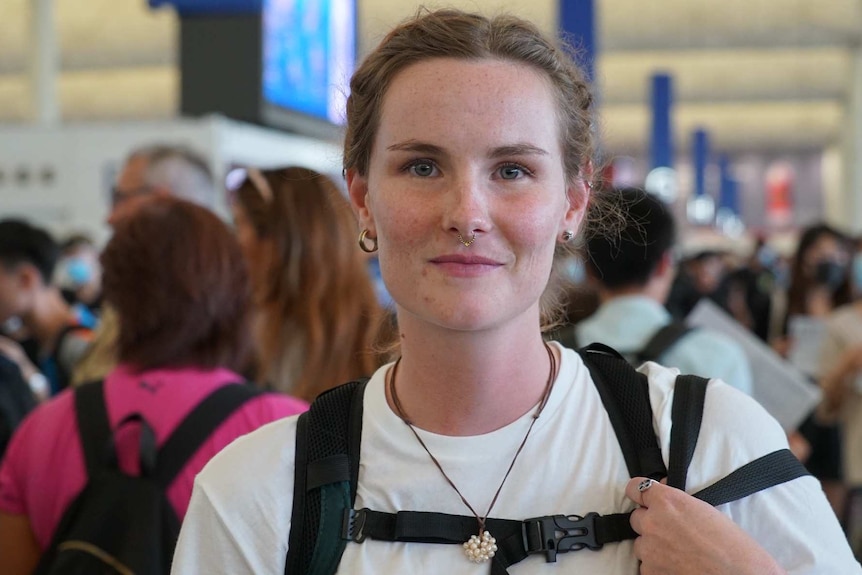 A young woman is holding a strap of her backpack while posing for a photo