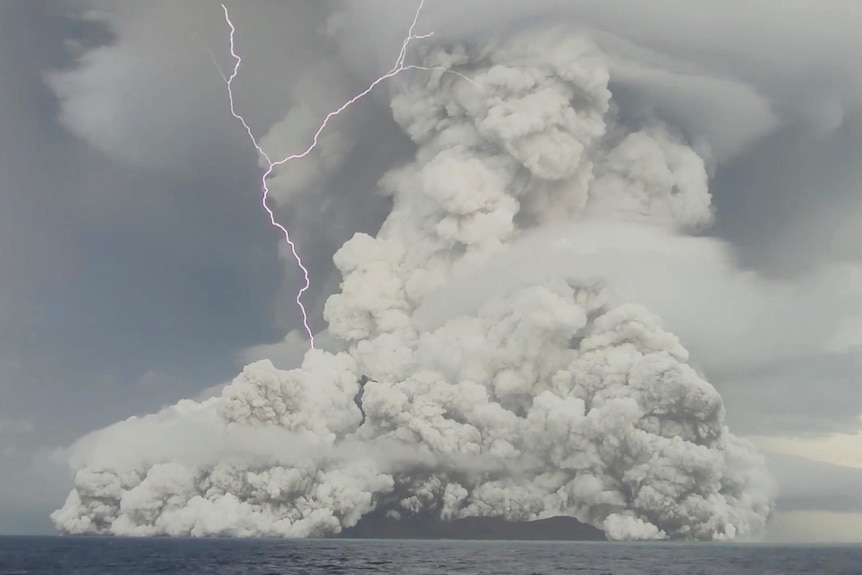 A huge grey cloud rises from a submarine volcano, as a forked bolt of lightnight hits the left side of the rising ash plume.