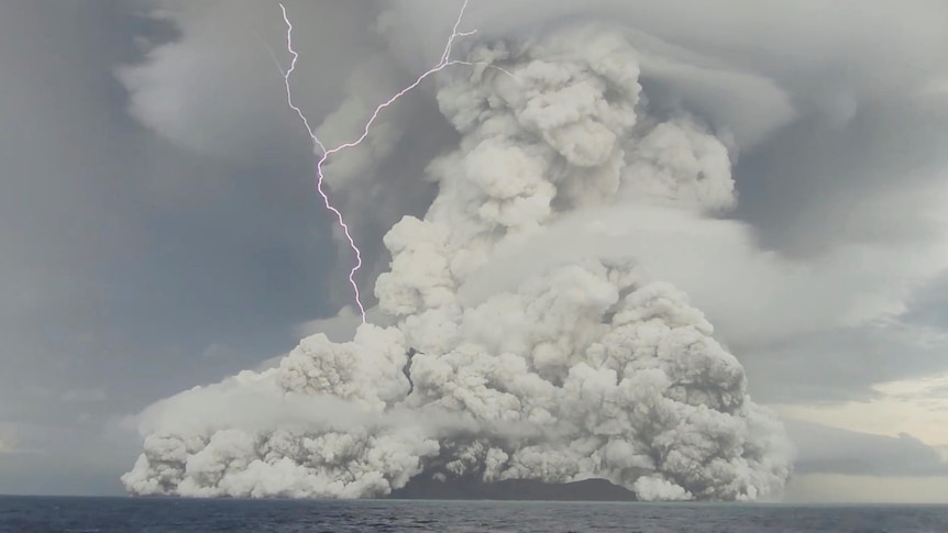 A huge grey cloud rises from a submarine volcano, as a forked bolt of lightnight hits the left side of the rising ash plume.