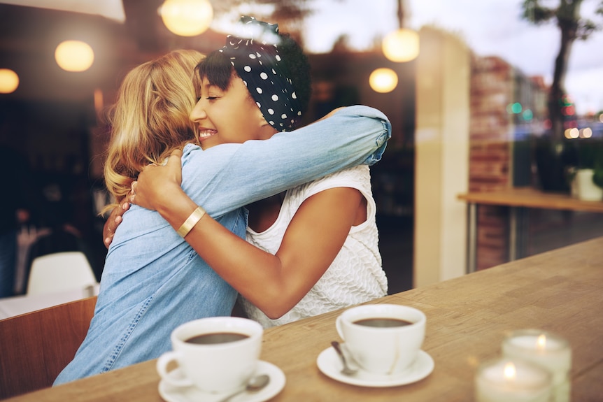 Two women hug each other tightly over coffee in a cafe