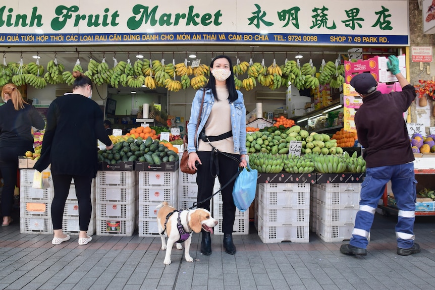 A woman wearing a mask stands outside a fruit and veg shop.