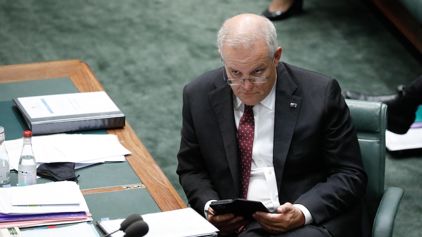 Scott Morrison looks over his glasses while reading something in the House of Represenatives