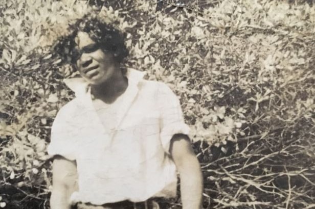 A black and white photo of a young Aboriginal man wearing a button up shirt and trousers