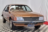 A brown old Holden sedan sits on a chequered showroom floor