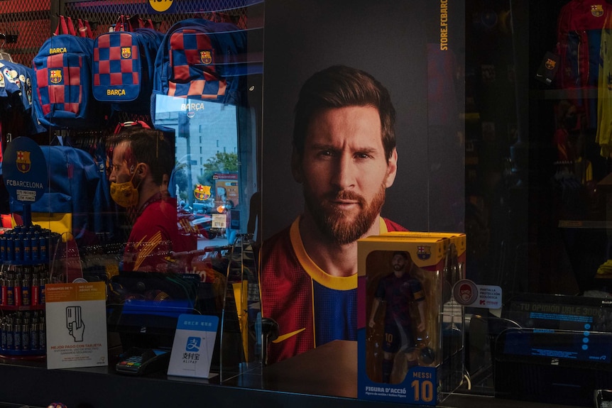 A Lionel Messi poster and action figure can be seen through a Barcelona team shop window.