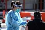 A nurse wearing protective equipment and face mask injects a seated patient at an outdoor vaccination centre.