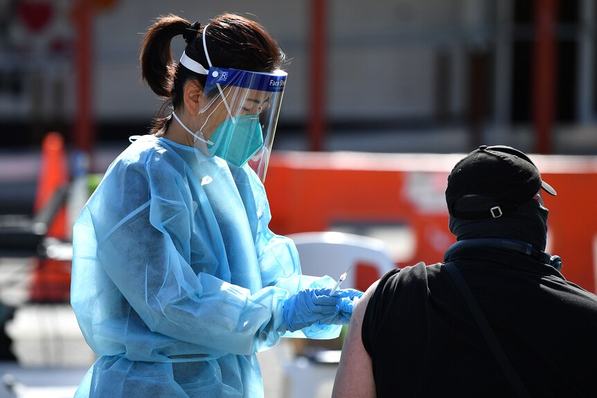 A nurse wearing protective equipment and face mask injects a seated patient at an outdoor vaccination centre.