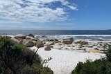 A photo of a beach with white sand and blue ocean with large boulders near the shore.