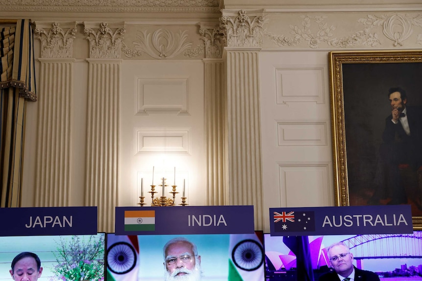 Three monitors with leaders of Japan, India and Australia in front of painting of Abraham Lincoln.
